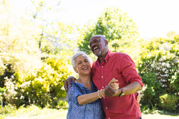 Happy diverse senior couple dancing in sunny garden