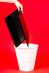 Black laptop in a trash bin on a red background isolated