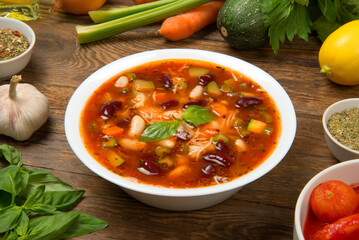 Italian minestrone soup in a white porcelain soup bowl on a rustic wooden table with ingredients. - 683273049