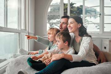 Parents, children and relax by window, happy and pointing with view, bonding and love with in family house. Father, mother and kids with conversation, talking and smile on bean bag, wow face and home - obrazy, fototapety, plakaty