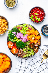 Vegan buddha bowl with baked pumpkin, quinoa, tomatoes, spinach, celery, radish, soybeans, edamame, tofu, cauliflower, broccoli and sesame seeds, white table background, top view. Autumn slow food