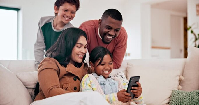 Happy, phone and children with parents on a sofa in the living room of modern family home. Laughing, having fun and young kids watching video on cellphone with interracial mother and father in lounge