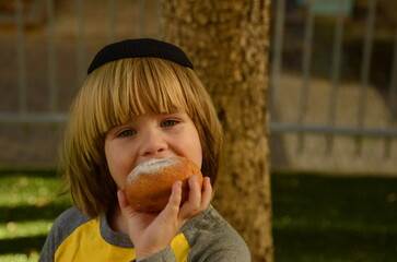 Jewish winter holidays - Hanukkah. The boy eats sufganiyot. Close-up - Sufganiyah donut with jam.