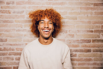 Portrait of a smiling young african american man with afro hairstyle with a brick wall background.