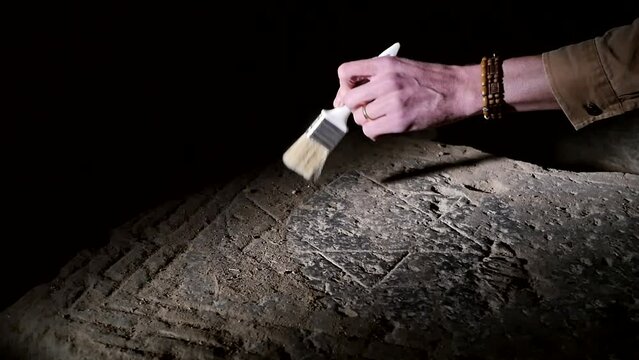 The hand of a male archaeologist uses a brush to clean dust from a stone slab depicting the ancient sign of the six-pointed Jewish Star of David. Historical find confirming the territory of the Jews