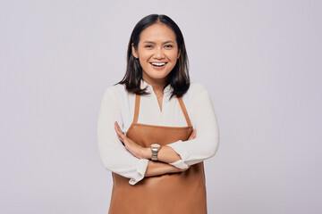 Optimistic young Asian woman barista employee in brown apron working in coffee shop, standing with crossed arms, looking on camera with smile isolated on white background. Small business startup
