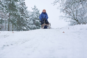 A happy child slides down a snowy hill on a wooden sled, winter fun during the holidays.