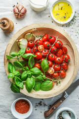 Italian food classics: tomatoes and fresh basil on wooden plate with other ingredients olive oil and garlic, top view