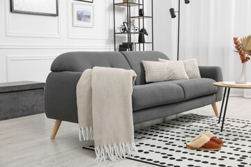Stylish living room interior with comfortable sofa, blanket, slippers and side table