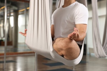 Man meditating in fly yoga hammock indoors, closeup
