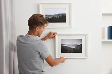 Fototapeta na wymiar Young man hanging picture frames on white wall indoors, back view