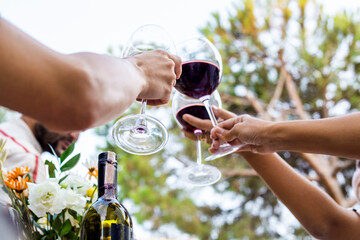 Close-up hands of people clinking glasses with red wine at outdoor party. Bottom view