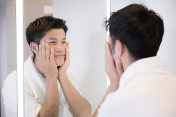 洗面台で洗顔などをして鏡を見たり髭を剃る男性　