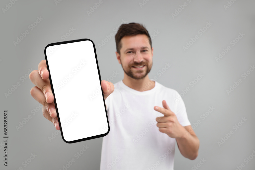 Poster handsome man showing smartphone in hand and pointing at it on light grey background, selective focus