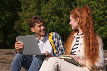 Happy young students studying with laptop together on steps in park