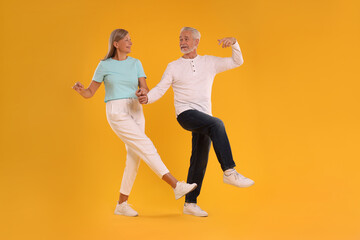 Fototapeta na wymiar Senior couple dancing together on orange background