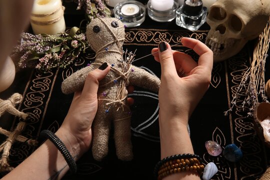 Woman stabbing voodoo doll with needle at table, closeup. Curse ceremony