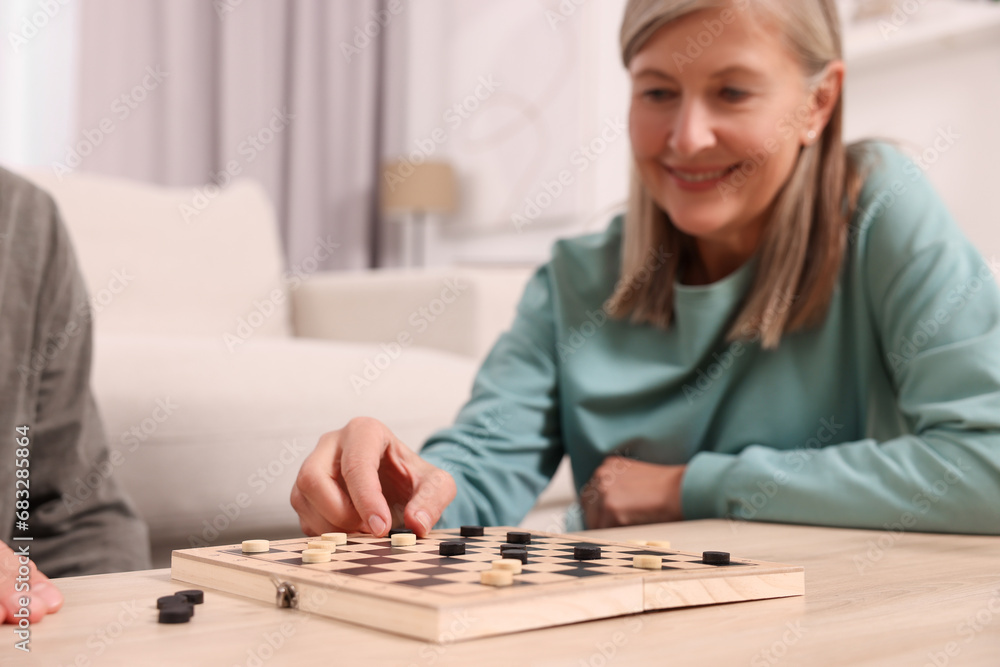 Poster People playing checkers at wooden table in room, selective focus