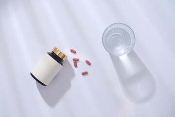 Top view of an unbranded medicine bottle, pills and a glass of water on a white background with...