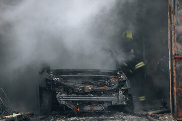 Firefighters extinguish a burning car in a garage. Burnt car. Rescuers. Strong smoke. Emergency....