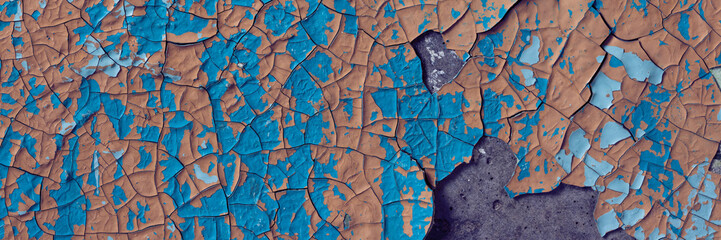 Peeling paint on the wall. Panorama of a concrete wall with old cracked flaking paint. Weathered rough painted surface with patterns of cracks and peeling. Wide panoramic grunge texture for background