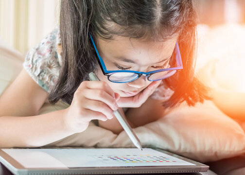 School child girl kid using internet online learning on mobile tablet reading looking at digital screen for educational study for Children’s Eye Health and Safety Month and Blue Light Awareness Day