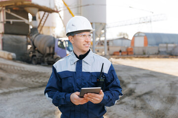 Engineer man in uniform use tablet computer for controls loading of cement to mixer truck on concrete factory. Concept automated industry logistics with online