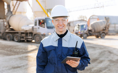 Modern technologies industrial cement plant concept. Engineer in uniform and hard hat uses tablet...