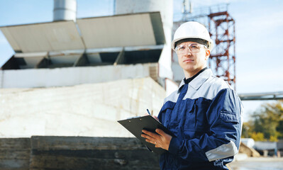 Builder worker in uniform with tablet working on heavy construction site at cement plant