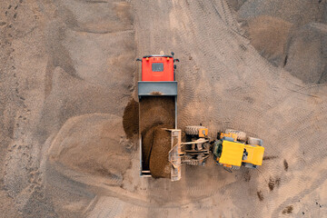 Aerial top view mining excavator loading sand in lorry truck in opencast. Open pit mine concept