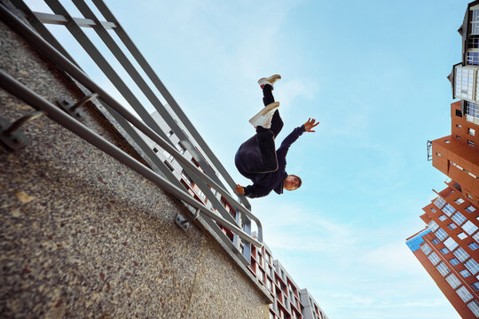 Athlete man, young guy jumping, flips of wall, practice Parkour in public park among high-rise buildings over sunrise. Eye fish filter.