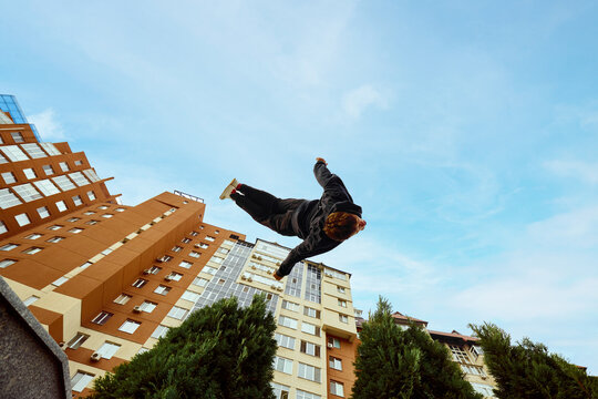 Athlete man, young guy jumping high, making back-flip over city, high-rise buildings and sky view in public park. Eye fish filter.