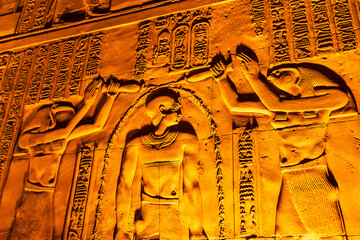 Carved walls of the Kom Ombo temple illuminated at night.