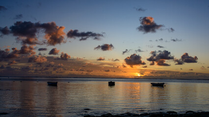 Golden sunrise on the east coast of Mauritius with small fishing boats on the foreground