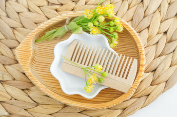 Small wooden plate with wooden hairbrush (comb) and linden (tilia, basswood, lime tree) flowers. Natural hair care, homemade spa and beauty treatment recipe.