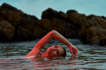 Woman enjoys serene swim in lagoon at dusk, nature's swimming pool, tranquil moment captured, wellness in natural habitat. - obrazy, fototapety, plakaty