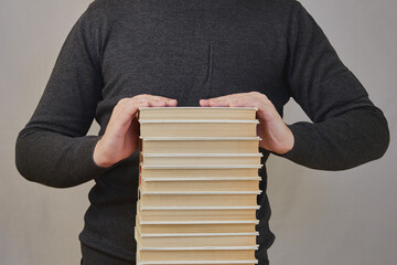 Student's hands are on top of a large stack of books. High academic workload at school, large...