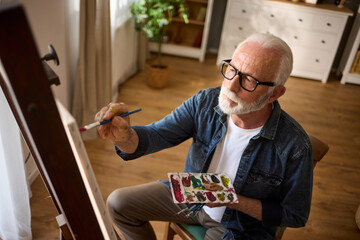 Elderly man painting on a canvas at home