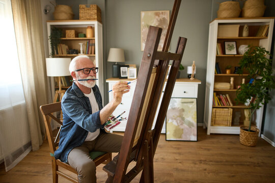 Elderly man painting on a canvas at home