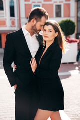 Beautiful fashion woman and her handsome elegant boyfriend in black suit. Sexy brunette model in jacket. Fashionable confident couple posing in street. Brutal man and female outdoors