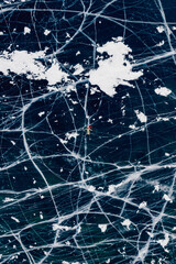 Woman tourist on ice skates and with long red scarf on frozen cracks lake Baikal, aerial top view