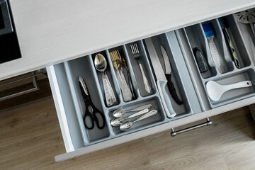 Open drawer in a kitchen, which is part of a white kitchen cabinet and sitting on a wooden floor....