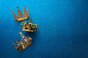 Epiphany Day or Dia de Reyes Magos concept. Three gold crowns on blue sparkling background - obrazy, fototapety, plakaty