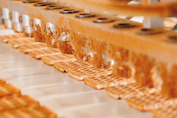 Caramel is applied Belgian waffles on conveyor production line. Automatic bakery plant food factory - obrazy, fototapety, plakaty