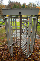 Revolving metal turnstiles secure acces gate entrance to a public park in a forest. Autumn colors, cloudy day, no people