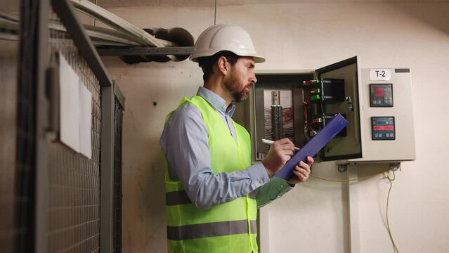 Portrait of a Professional Industry Electrical Engineer Worker Wearing Safety Uniform and Hard Hat Uses Tablet for Data Analysis. Confident Male Industrial Specialist Standing in a Factory Facility.