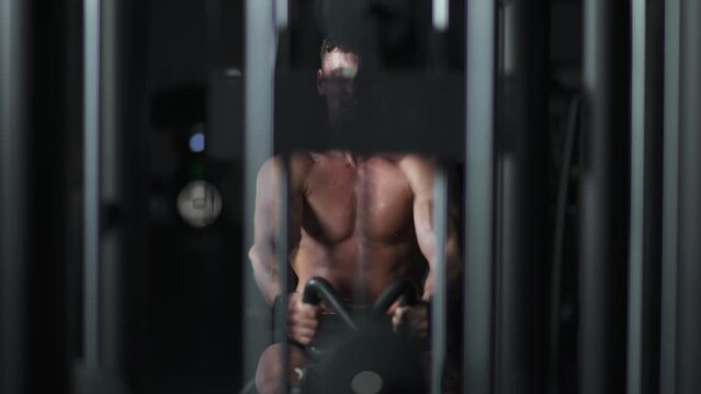 Athletic man in the Gym lifting blocks on rowing machine, training on block device and gym equipment, night time.