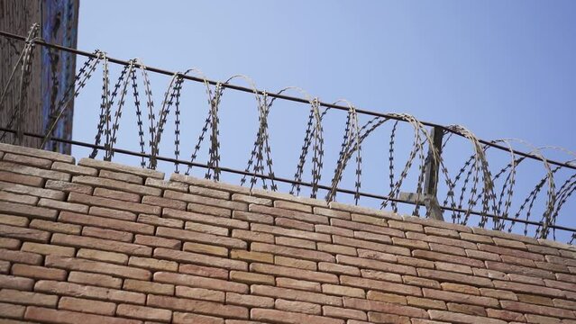 A brick wall with a security wire fence. A jail wall from above. Outdoor. Prison yard. Freedom, war, forbidden, crime, protection, dangerous, control, escape concepts.