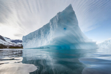 The image captures a massive iceberg floating in icy waters, its jagged edges reflecting sunlight....