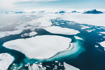 The image captures a breathtaking aerial view of icebergs floating on the ocean in the Arctic. The...
